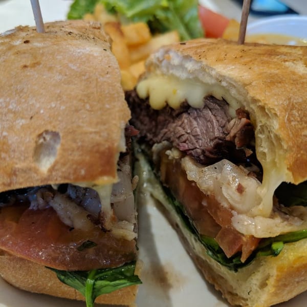 Victoria's Diner steak sandwich with melted cheese, tomatoes, and spinach, served with fries and salad.