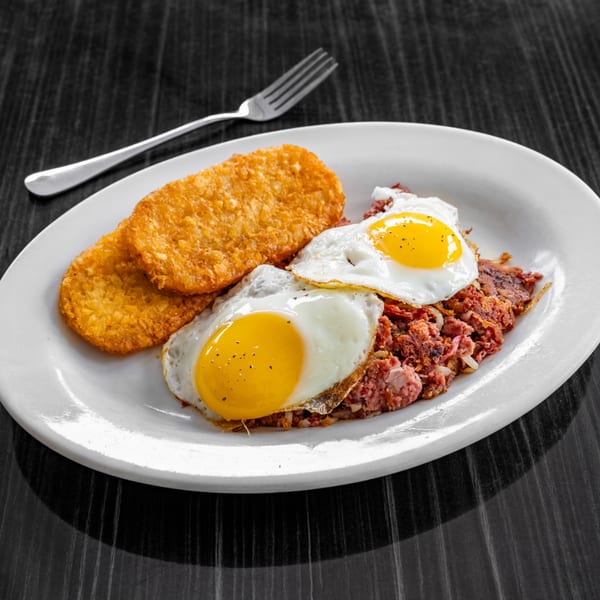 Victoria's Diner corned beef hash with two fried eggs and two hash browns on a white plate.